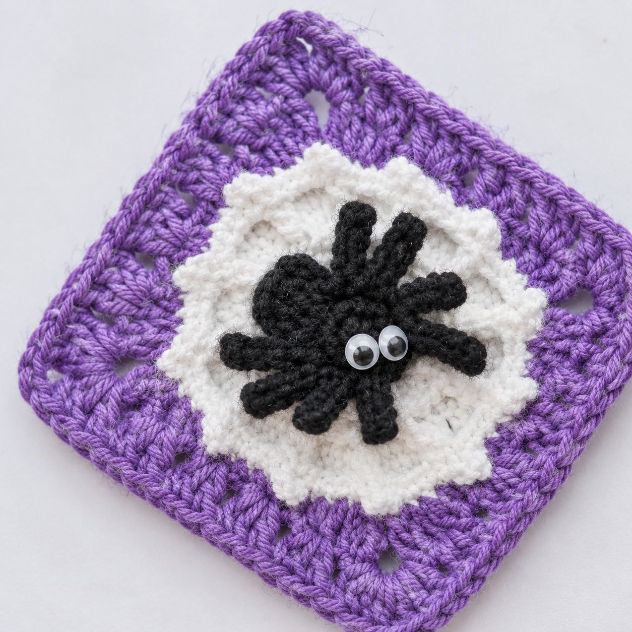 Close-up of one spider granny square on a white background, showing the eight legs, the white web behind them and the granny-square border