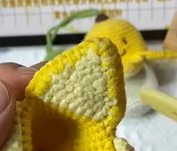 One yellow crocheted flap seen from the back, its light yellow lining edged round in yellow, with a finished banana out of focus behind