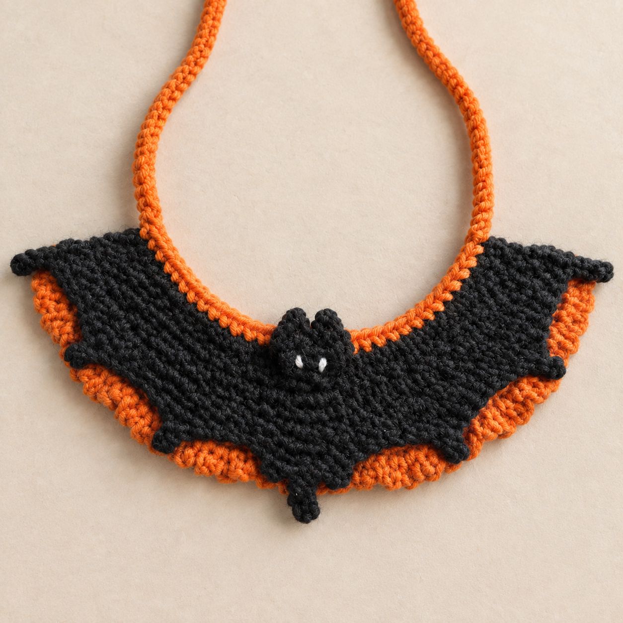 The bat collar seen from above on a cream background, with the orange ties curving up out of the frame