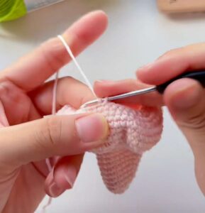 The pink body of a crocheted starfish held upside down, its pointed top hanging below and the hook in the stitches round its open end