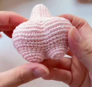 The pink body of a crocheted starfish held in two hands with both short legs worked and closed, the seat rounded between them and the pointed top above