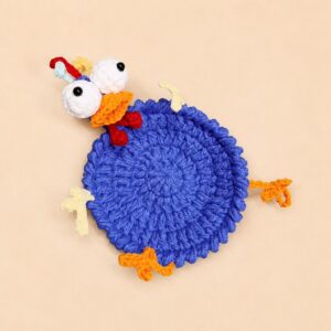 The finished blue chicken coaster seen from above, a thick crocheted disc with a raised corded rim, two round white eyes with black bead pupils, a folded orange beak with a red piece under it, three thin red, pale blue and yellow pieces on the crown, two pale yellow and two orange claw-shaped pieces around the edge
