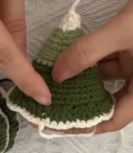 A green crocheted tree held in two hands with its lowest tier of leaves on: green scallops edged in cream, folded down towards the base, and a cream tip at the top