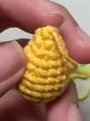 A stuffed yellow crocheted body, narrowing towards the top, held between finger and thumb