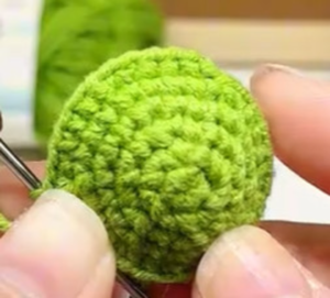 A flat round green circle of single crochet held in the fingers, a crochet hook still in its edge and a ball of green yarn behind it