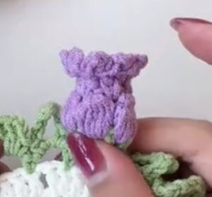 A finished lilac crocheted lily, a small bell with picots round its rim, standing up from the green leaf edging