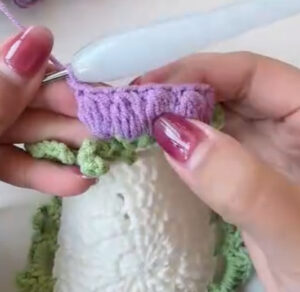 A lilac lily's clusters being crocheted onto one green scallop at the edge of a white coaster centre