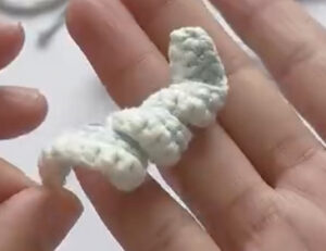 A pale crocheted tentacle, one row of single crochet along a chain, twisting into a loose curl across the fingers of a hand