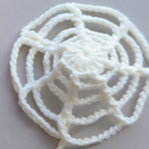 A round white crocheted web laid flat on a grey surface, rings of chain arches spreading out from a solid centre