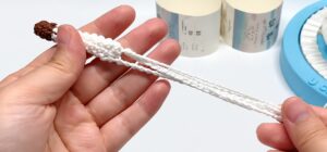 The crocheted tail held in one hand, white with a chestnut tip, and its long white chain loop pulled out straight to the other hand