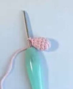One small pink crocheted arm, a rounded bobble, still on the hook with its tail hanging