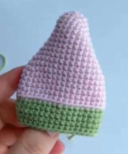 The pink body of a crocheted key pouch held up in the fingers, a pointed triangle with a green band along the bottom and a thin pale line where the colours meet