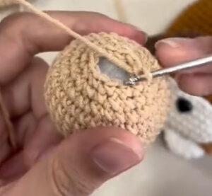 A tan crocheted ball for a puppy's head on the hook, a little white filling showing through the small opening at the top