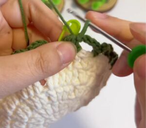 Green chain loops being crocheted round the edge of a cream coaster centre, the hook still in the work