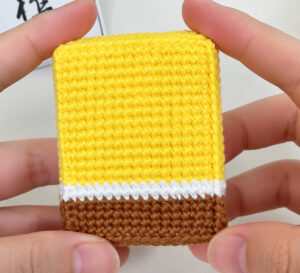 The body closed into a box and held in two hands: a yellow front with a white band and a brown band along the bottom