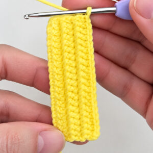 The flat top of the body, a long yellow rectangle worked in rows, held in the fingers with the hook still in it