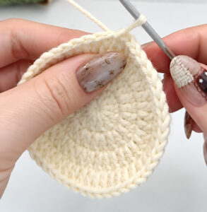 A flat cream disc of crocheted double crochet held in the fingers, a grey crochet hook still in its edge with the working yarn running up from it