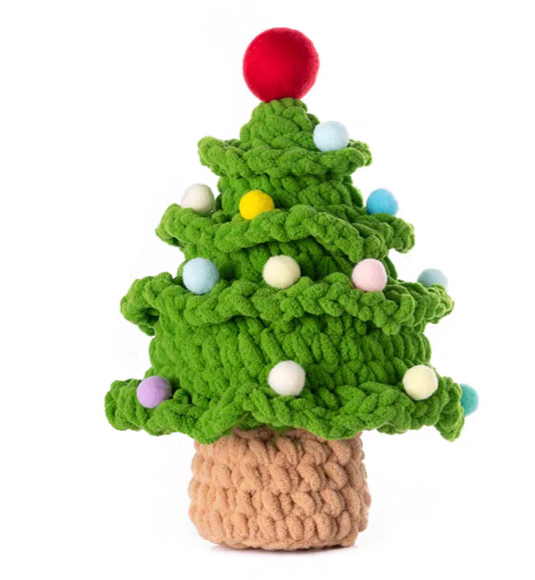 A crocheted Christmas tree in green chenille on a white background: four tiers of ruffled frills, small pompoms in white, pale blue, pink, yellow and lilac, a red ball on top, and a short light brown trunk